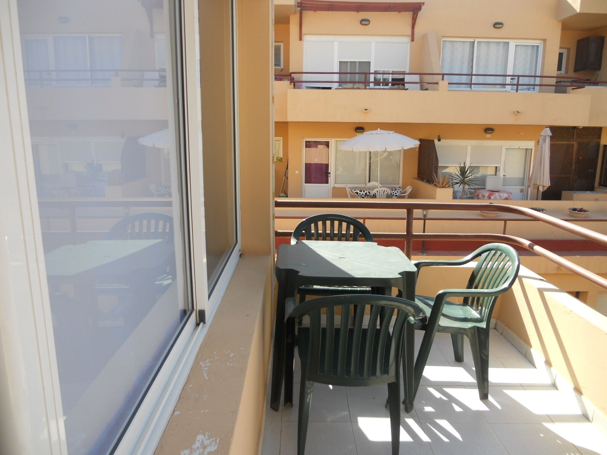 A balcony with a table and chairs, a railing, and a view of the building's interior.