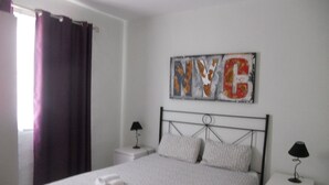 A bedroom with a bed, two bedside tables, a wall art piece, and a window with curtains. - Lovely Apt Siesta (La Oliva)
