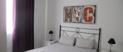A bedroom with a bed, two bedside tables, a wall art piece, and a window with curtains.