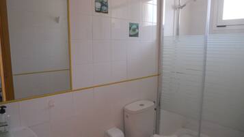 A bathroom with a toilet, a sink, a shower, and a mirror.