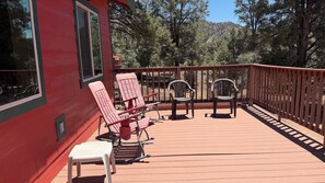 A deck with chairs and a table, surrounded by a wooden railing and trees.