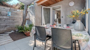 Um pátio externo com uma mesa posta para refeições, cercado por cadeiras e um vaso de planta.