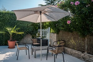 An outdoor patio with a table and chairs, a large umbrella, and a potted plant.