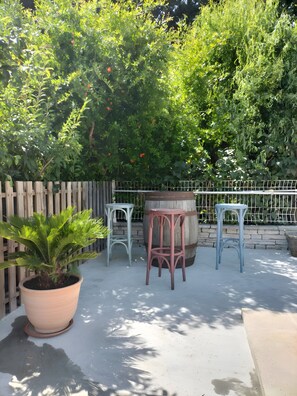 Un espace patio agrĂ©mentĂ© dâune clĂŽture en bois, dâun grand pot de fleurs, de deux tabourets de bar en mĂ©tal et dâun tonneau en bois.