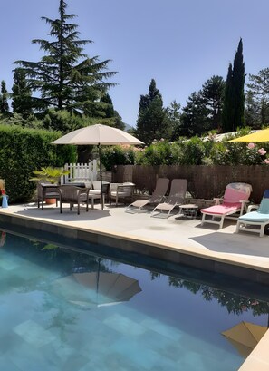 Un espace aménagé au bord de la piscine, avec des chaises longues, une table et des parasols.