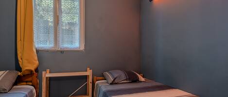 A bedroom with two single beds, a window with lace curtains, and a wall-mounted light fixture.