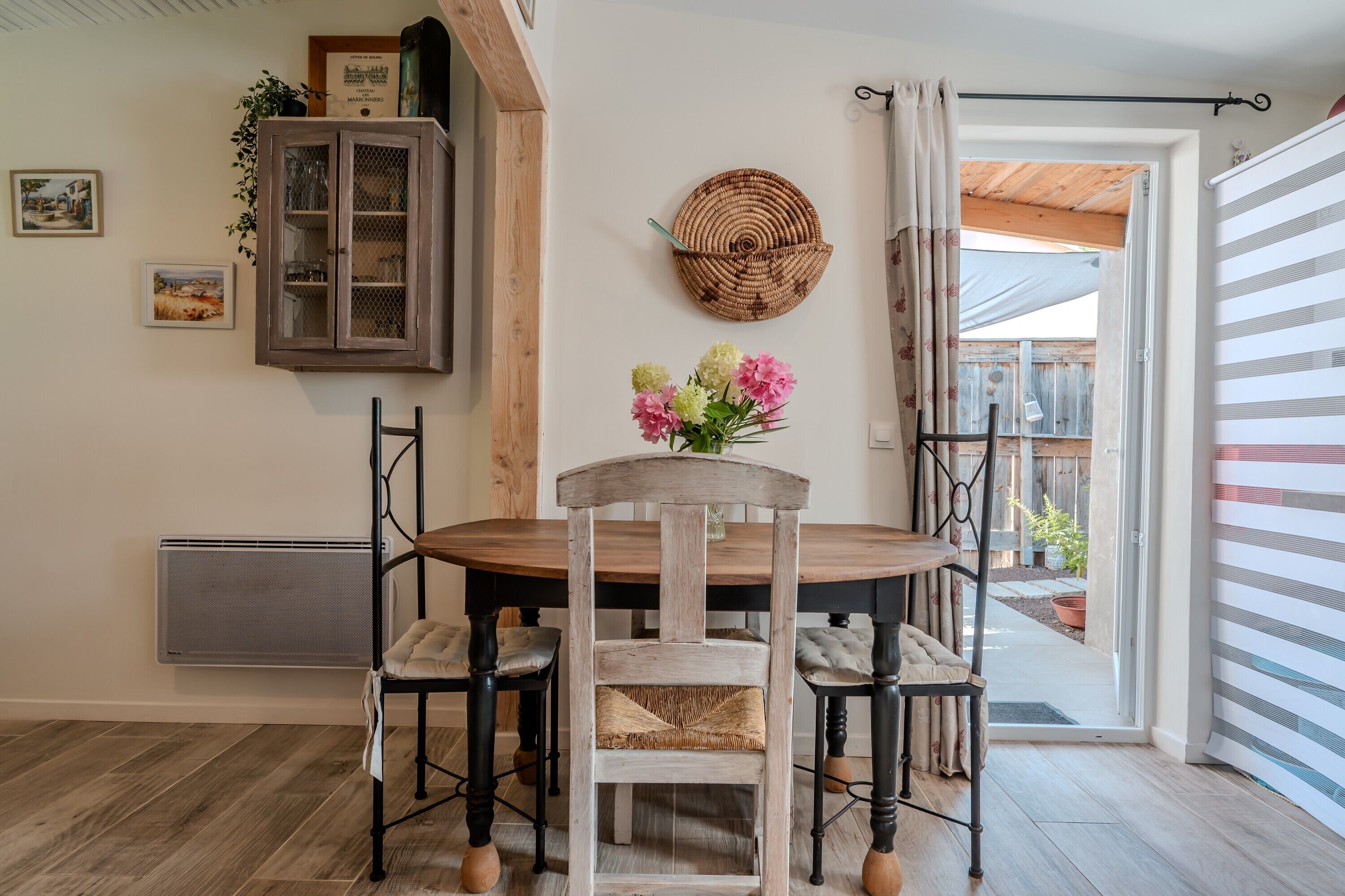 A dining area with a wooden table and chairs, a cabinet with glass doors, and a woven wall hanging.