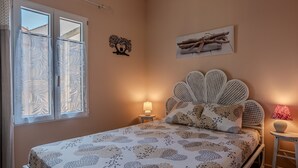 Quarto com cama, duas mesinhas de cabeceira, janela com cortinas e decoração na parede.