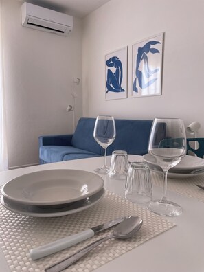 A dining area with a white table set for two, including plates, glasses, and cutlery. - Studio apartment in the center of Badesi with shared pool (Badesi, provincia di Sassari)
