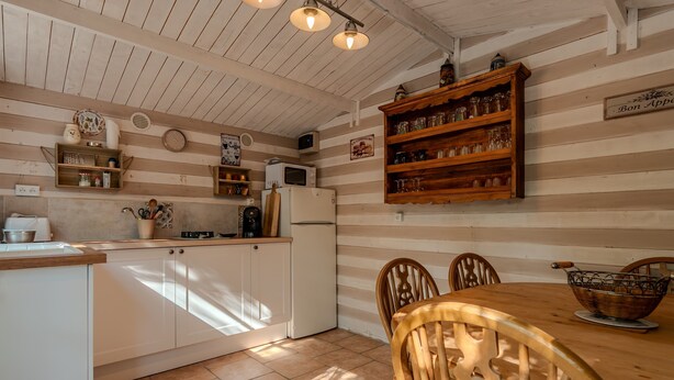 Una cocina con armarios de madera, refrigerador, microondas y una mesa de comedor con sillas.