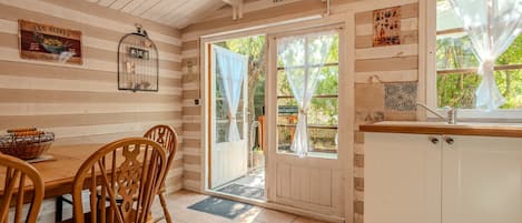 A wooden interior with a dining table, chairs, a kitchen area, and a large window with curtains.