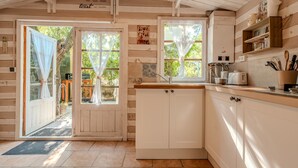 Una cocina rústica con paredes de madera, horno empotrado y ventana con cortina ligera.