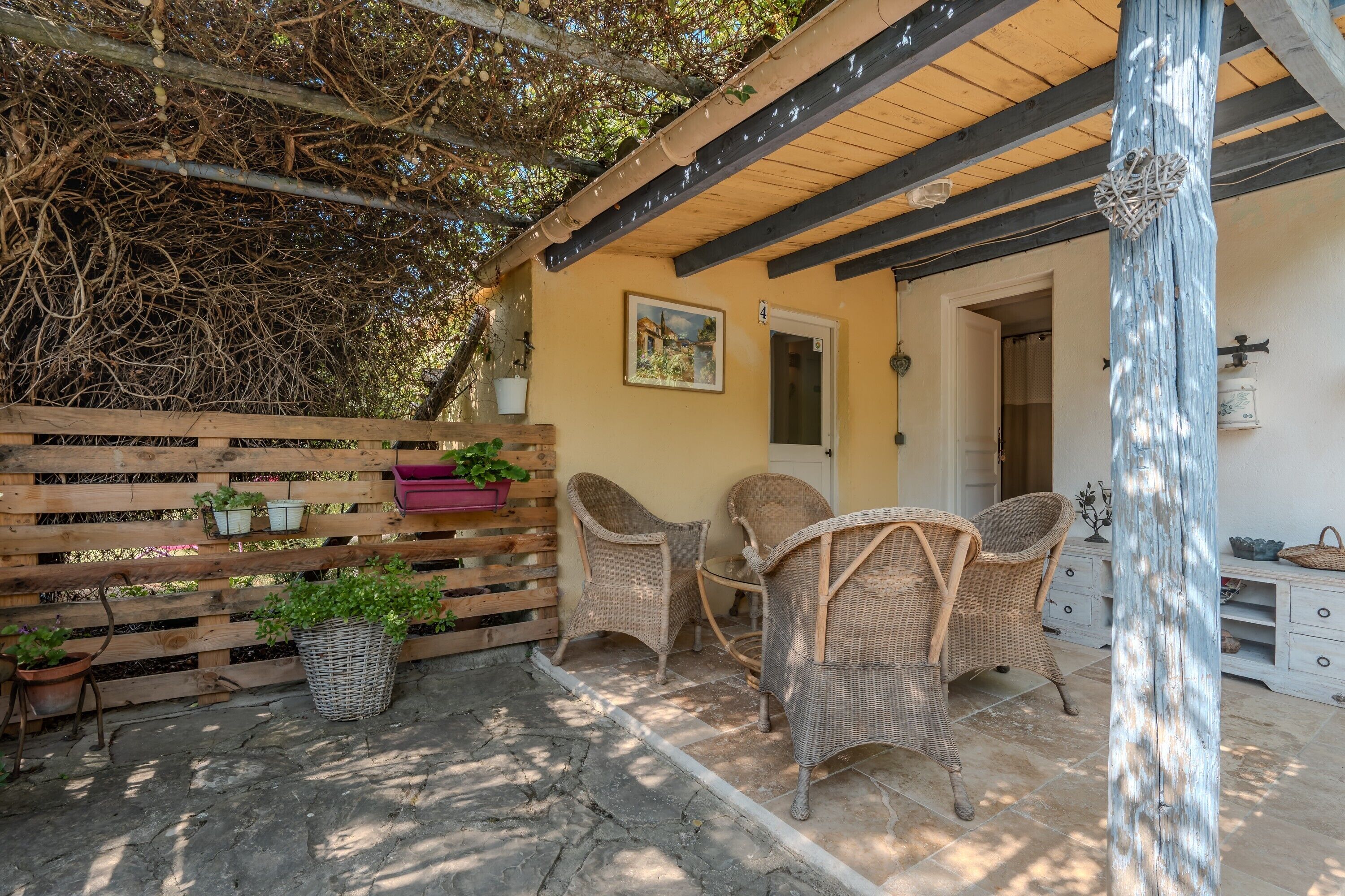 A covered patio area with wicker furniture, a wooden fence, and potted plants.