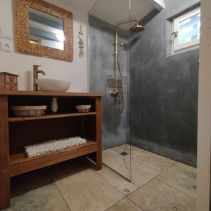 A bathroom with a wooden vanity, a large mirror, a white sink, a shower with a glass door, and a window.