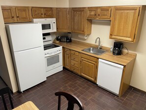 A compact kitchen with wooden cabinets, a white refrigerator, a microwave, a stove, a sink, and a dishwasher.
