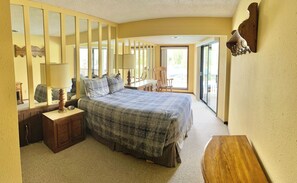 A bedroom with a large bed, a nightstand, a dresser, a chair, and a mirror.