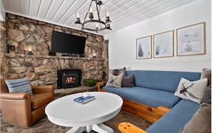 Ein gemütliches Wohnzimmer mit Kamin aus Stein, einem blauen Sofa, einem braunen Ledersessel und einem runden weißen Tisch.