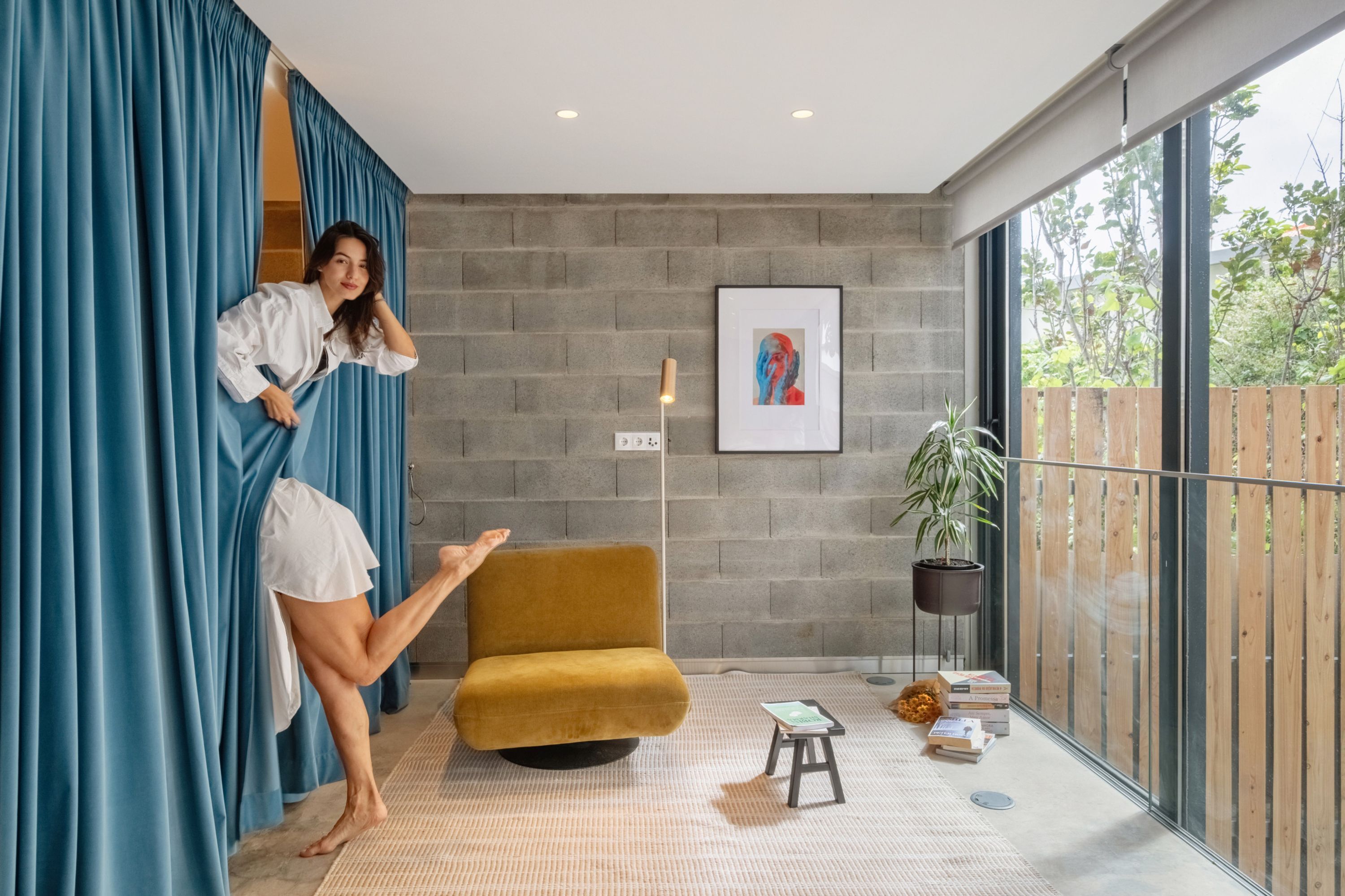 Une pièce moderne avec une grande fenêtre, une chaise jaune, un petit tabouret et une plante en pot.