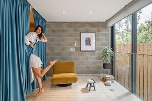 Ein modernes Zimmer mit einem großen Fenster, einem gelben Sessel, einem kleinen Hocker und einem Blumentopf.