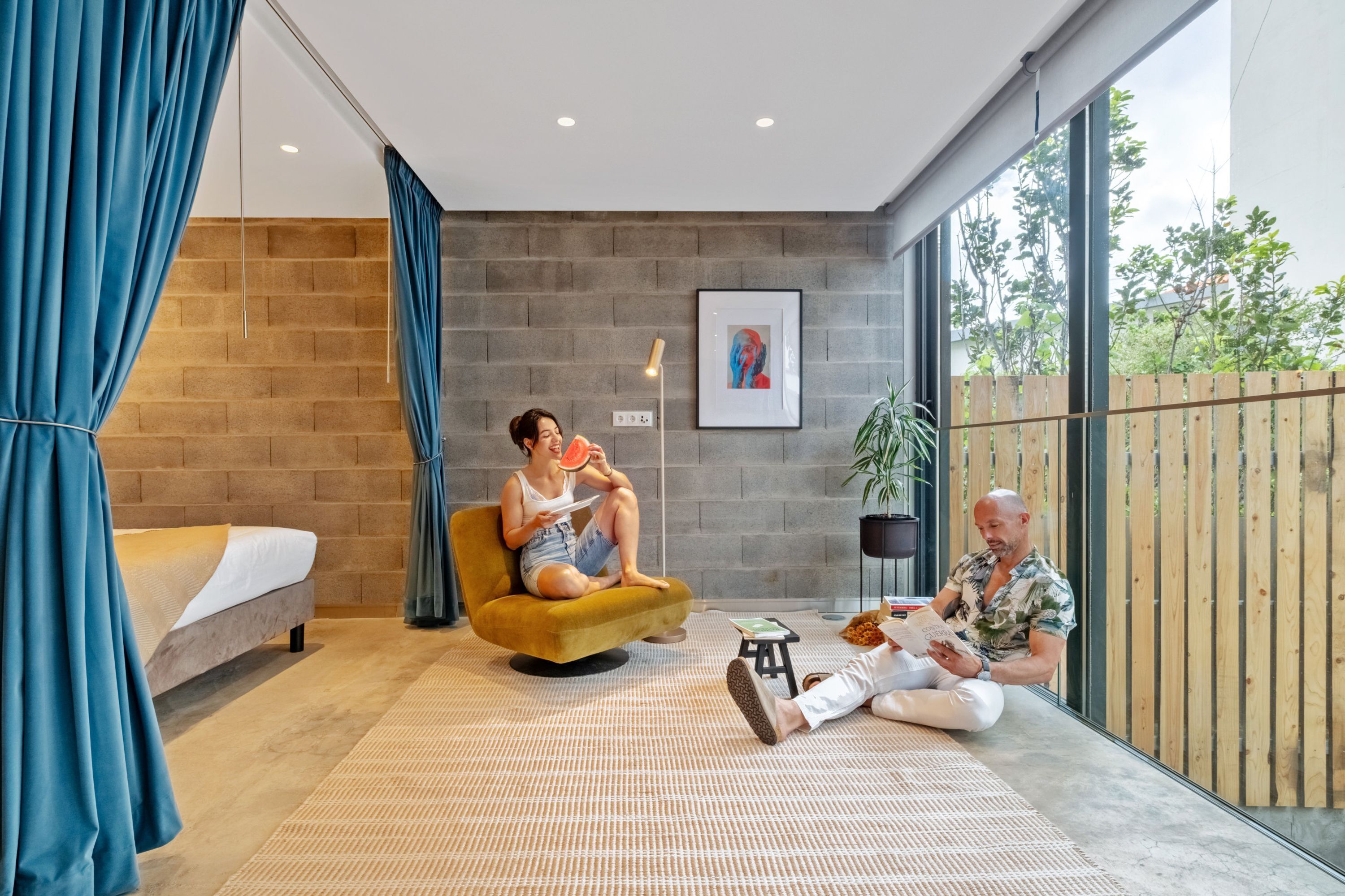 Ein modernes Zimmer mit Backsteinwand, einem Bett, einer Couch, einem kleinen Tisch und einem großen Fenster.