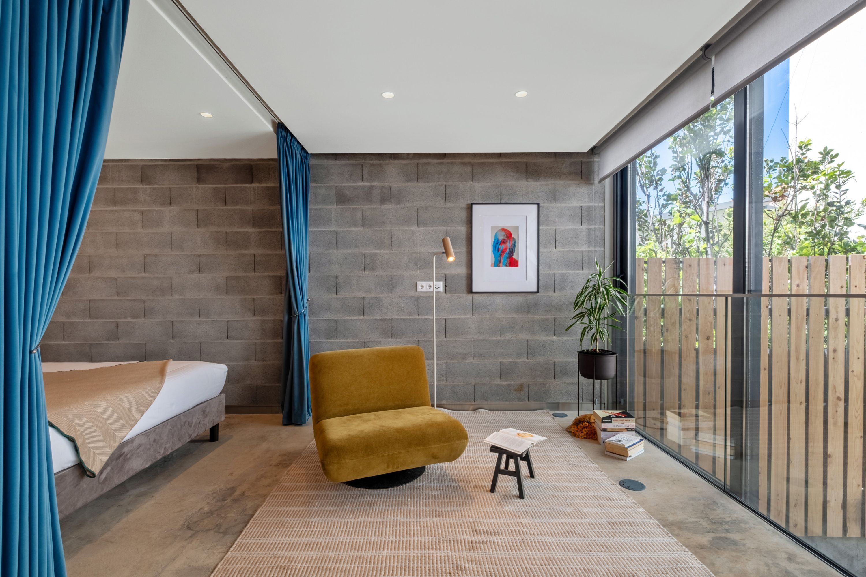 Une chambre moderne avec un lit, un canapé, une petite table, une plante en pot et une grande fenêtre.