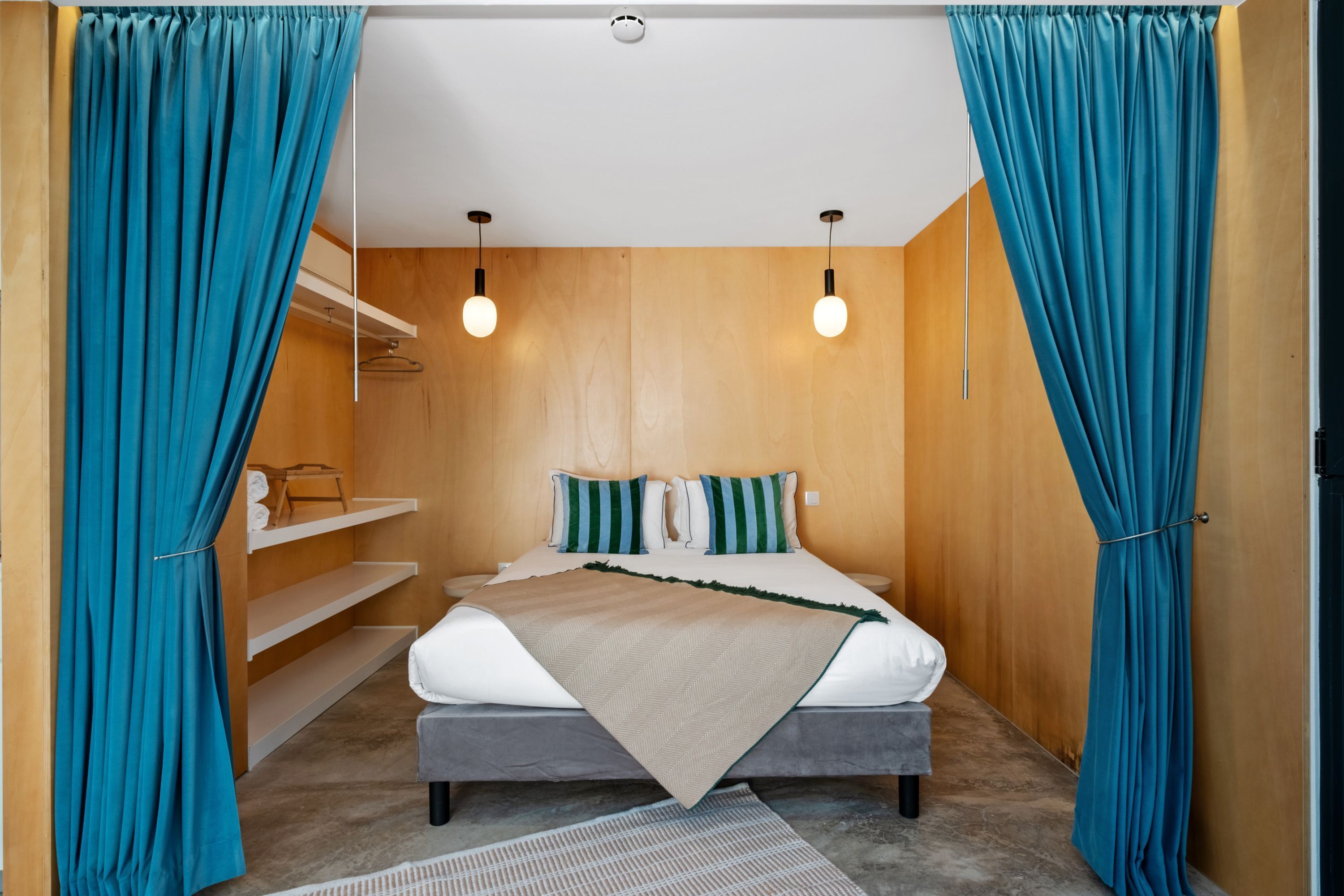 A bedroom with a bed, curtains, a shelf, and a hanging light fixture.