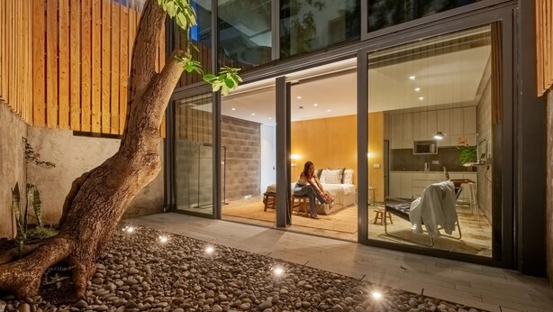 A modern interior with a large glass door leading to a bedroom, a kitchen area, and a small outdoor space with a tree and pebbles. - The 21 - Gaia by Homie (Ribeira Brava)