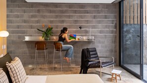 A modern room with a brick wall, a desk with a laptop, a chair, a small table, and a large window. - The 21 - Gaia by Homie (Ribeira Brava)