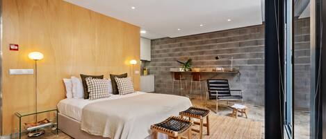 A modern bedroom with a large bed, bedside lamps, a small table, and a seating area with stools.