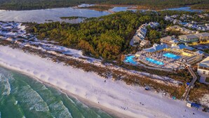 Vista aérea de um resort à beira-mar, com ampla área de piscina, praia e extensa área arborizada.