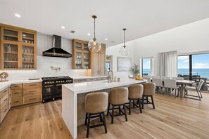 A modern kitchen with a large island, wooden cabinets, and a view of the ocean. - Gulf Front Retreat with Pool and Peleton (North Cape San Blas)