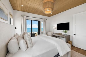 A bedroom with a large bed, a desk, a TV, and a view of the sea. - Gulf Front Retreat with Pool and Peleton (North Cape San Blas)