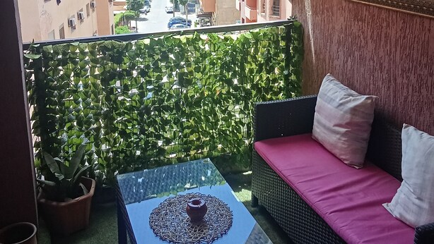 Un balcon avec un canapé en osier, une table en verre et une vue sur une rue de la ville.