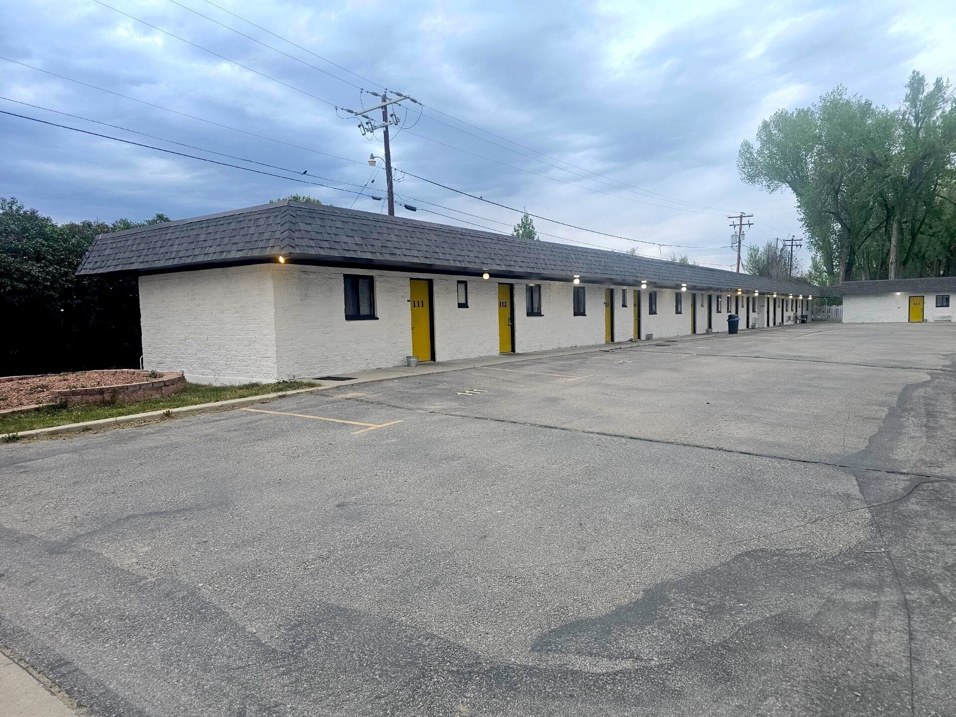 A row of motel rooms with individual doors, a parking lot, and a utility pole with power lines.