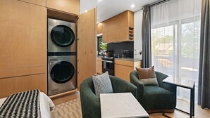 Een compacte hotelkamer met een kitchenette, een bank, een eettafel en een groot raam.