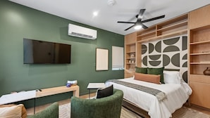 Een moderne slaapkamer met een bed, een bureau, een stoel, een televisie en een plafondventilator.