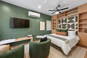 A modern bedroom with a bed, green upholstered chairs, a desk, a flat-screen TV, and a ceiling fan.