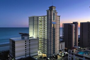 A high-rise hotel with multiple floors, a pool area, and a view of the ocean.