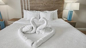 Una habitació d'hotel amb un llit ben fet, un tabernacle de fusta, roba de llit blanca i una làmpada a la nit.