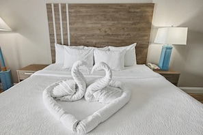 A hotel room with a neatly made bed, a wooden headboard, white bedding, and a lamp on the nightstand. - Oceanfront King Room + Lazy River & Hot Tub (Myrtle Beach)