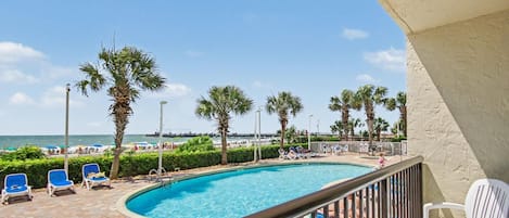 A pool area with lounge chairs, a clear view of the beach, and a distant pier.