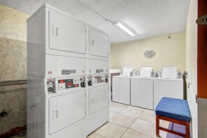 A laundry room with four stacked washers and dryers, a blue bench, and a wall sign indicating the room's purpose. - Oceanfront Two Queen Room + Lazy River & Hot Tub (Myrtle Beach)