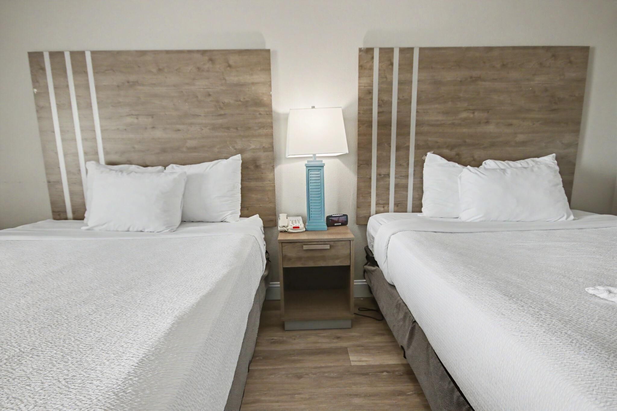 A hotel room with two beds, a nightstand with a lamp, and a wooden headboard.
