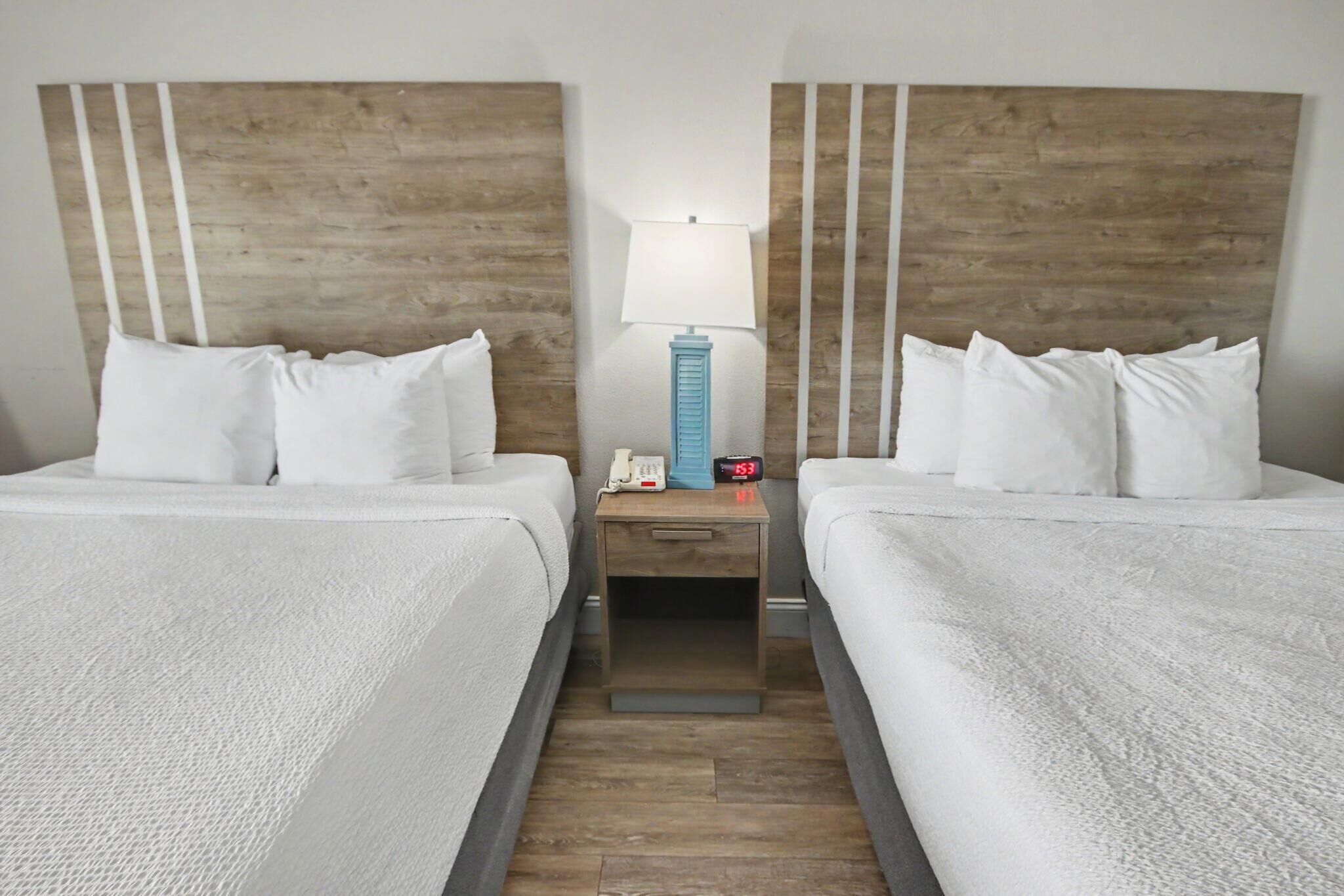 Habitació d'hotel amb dos llits, una tauleta de nit amb una làmpada, un telèfon i un rellotge digital.