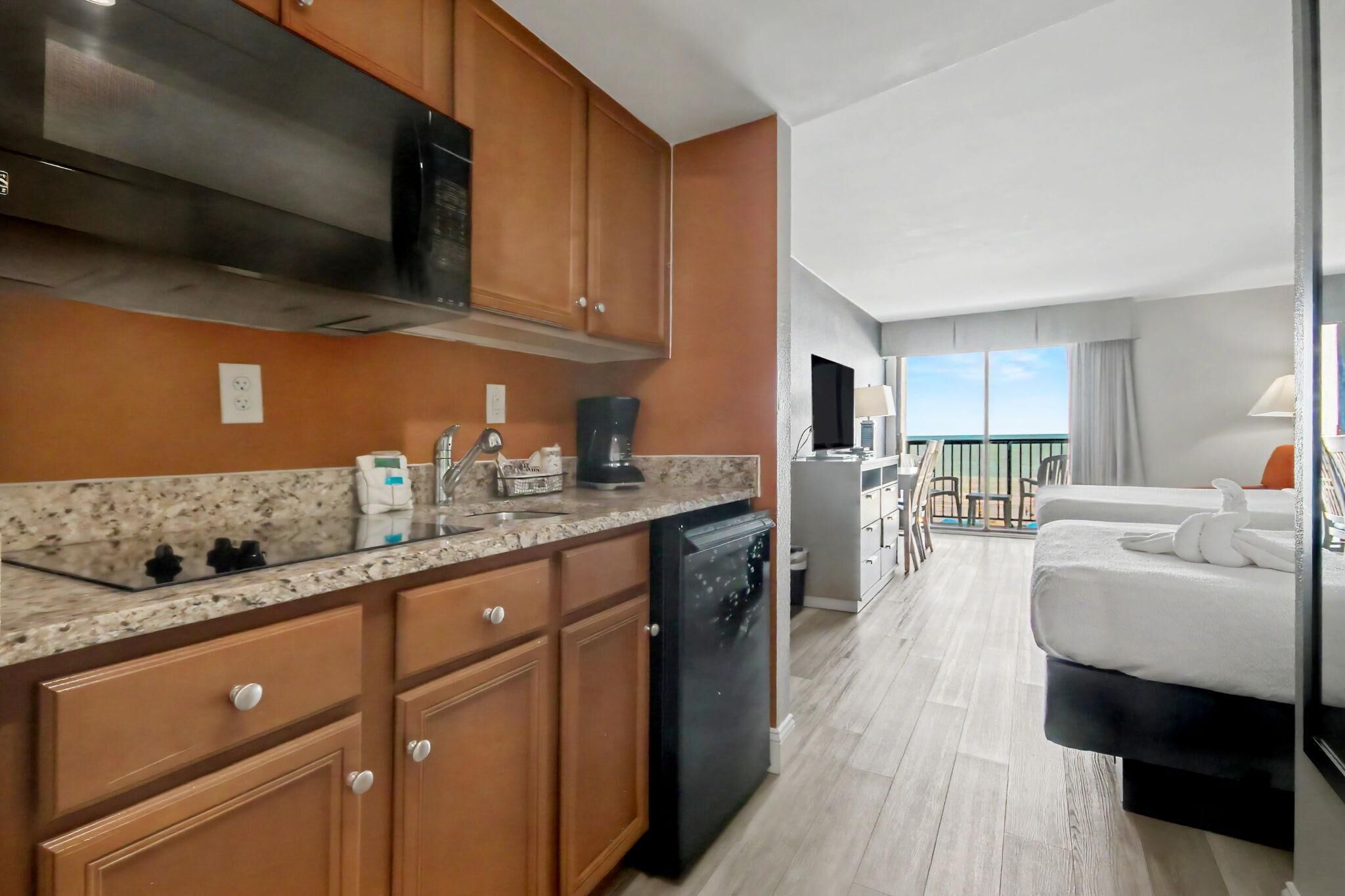 A hotel room with a kitchenette, a bed, a balcony with a view, and a TV.
