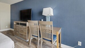 A bedroom with a bed, a dresser, a desk with a lamp, and a TV on the wall. - Oceanfront Two Queen Room + Lazy River & Hot Tub (Myrtle Beach)
