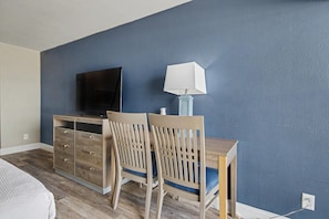 A bedroom with a bed, a dresser, a desk with a lamp, and a TV on the wall. - Oceanfront Two Queen Room + Lazy River & Hot Tub (Myrtle Beach)