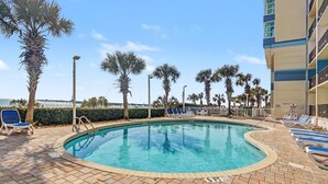 A pool area with lounge chairs, palm trees, and a view of the ocean. - Oceanfront Two Queen Room + Lazy River & Hot Tub (Myrtle Beach)