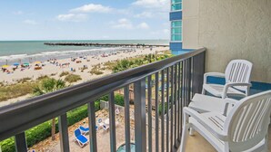 A balcony with a view of a beach, outdoor seating, and a pier in the distance. - Oceanfront Two Queen Room + Lazy River & Hot Tub (Myrtle Beach)
