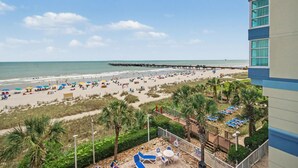 A beach with a pier, lounge chairs, and umbrellas. - Oceanfront Two Queen Room + Lazy River & Hot Tub (Myrtle Beach)